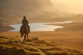 Person riding a horse in beautiful Irish landscape on dramatic sunset. Man admiring scenic view while on horseback riding tour in