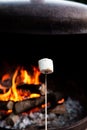 Person roasting over fire flames a marshmallows over campfire at night on a summer day, for smores or snack