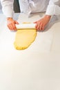 A pastry chef is rolling out dough on a table with a rolling pin. yellow dough and the worker is wearing a chef& x27;s uniform Royalty Free Stock Photo