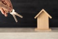 A person's hand holding the keys to their new home ownership with small wooden house in the background. Royalty Free Stock Photo