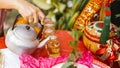 Person`s hand is holding stainless steel teapot to pour tea into mug that is set on a table covered with red cloth for good Royalty Free Stock Photo