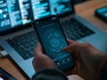 A person\'s hand is interacting with a smartphone displaying a cybersecurity lock graphic, with a laptop screen - ai. Royalty Free Stock Photo