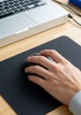 A person\'s hand, likely male, is using a computer mouse on a black mouse pad. The mouse is black Royalty Free Stock Photo