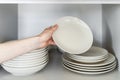 Person`s hand stacking white ceramic plates after washing