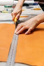 Person`s hands using cutting tool and metal ruler while producing leather goods