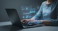 A person, seated at a table, engages with a laptop displaying futuristic,