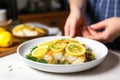 a person serving a plate of baked cod with lemon
