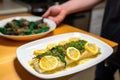 a person serving a plate of baked cod with lemon