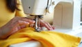Person sews yellow fabric with sewing machine. Close-up view of needle, thread, process of making clothes. Tailoring, Royalty Free Stock Photo