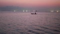 Person on shallop between lights of fishing ships in sea at sunset. Picturesque view of silhouette shipping on shallop