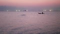 Person on shallop between lights of fishing ships in sea at sunset. Picturesque view of silhouette shipping on shallop