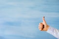 Person showing thumbs up hand gesture on empty blue background Royalty Free Stock Photo