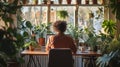 Person sits at a desk in a greenhouse surrounded by lush plants, experiencing a tranquil work environment.