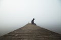 Person sitting on dock early morning with fog in the sky