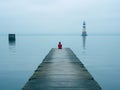 a person sitting on the end of a pier looking at a lighthouse