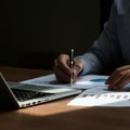A person is sitting at a wooden desk, analyzing documents with graphs and charts, Royalty Free Stock Photo