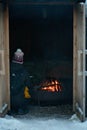 Person sitting in a wooden hut next to a campfire and warming up. Hut\'s doors are open and flames in the campfire burn Royalty Free Stock Photo