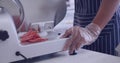 Person slices salami on a meat slicer at a deli