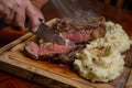 person slicing into a mediumrare steak next to mashed potatoes