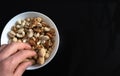 Person snacking a mixture of nuts peanuts, pistachios, almonds, walnuts, hazelnut, cashew in a bowl from top view with black Royalty Free Stock Photo