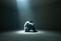 Person in solitude sitting alone in dark space, illuminated by a single ray of light Royalty Free Stock Photo