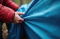 Person spreads blue tarp outdoors. Outdoor camping setup. Person preparing shelter for night. Nature background. Autumn forest.
