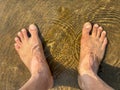 A person is standing barefoot in the sand with their feet in the water Royalty Free Stock Photo