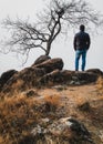 A person standing besides a barren tree on the top of a small hill. Self portrait of a person wwith rustic orange landscape Royalty Free Stock Photo