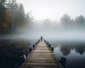 Person is standing at the end of long wooden dock on foggy lake in the fall. Royalty Free Stock Photo