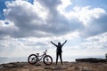 A person standing with hands up beside a bicycle on rocky mountain Royalty Free Stock Photo