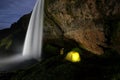 A person standing next to illuminated tent at beautiful Seljalandsfoss waterfall at night in Iceland Royalty Free Stock Photo