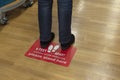 Person standing on Six Feet Apart Social Distancing red floor sign in a public building store Royalty Free Stock Photo