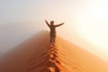 Person standing on top of dune in desert and looking at rising sun in mist with hands up, travel in Africa Royalty Free Stock Photo