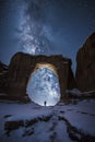 A person stands beneath a massive stone arch, gazing at a starry night sky, evoking a sense of wonder and insignificance