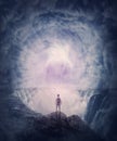 Person stands on the edge of a cliff above a waterfall looking at a huge whirlwind in the clouds that creates a portal to another