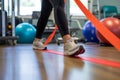 A person stands with a pair of orange tape wrapped securely around their ankles, A patient using a resistance band for physical