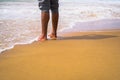 Legs of a person standing on the sandy shoreline against the lapping waves Royalty Free Stock Photo