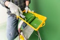 Person on a stepledder in working gloves holding yellow paint trough with middle-sized paint roller with green paint in front of