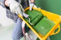 Person on a stepledder in working gloves holding yellow paint trough with middle-sized paint roller with green paint in front of