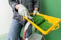 Person on a stepledder in working gloves holding yellow paint trough with middle-sized paint roller with green paint in front of