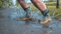 Person with striped rain boots jumping in a puddle of water, water splashing around on asphalt ground, grass and early autumn Royalty Free Stock Photo