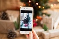 Person takes a photo on a smartphone of christmas tree with a christmas background