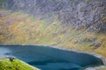 Person taking a photo of a huge valley with green hillside and blue lake in the mountains of Snowdonia, Wales