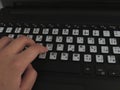 A person typing on a laptop using an Arabic keyboard.