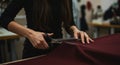 A person is using large fabric scissors to cut a piece of dark red cloth on a table.