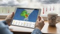 Person using tablet to check weather forecast with rain and clouds outside Royalty Free Stock Photo