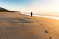 A person walking on a beautiful beach leaves a trail of footprints as the golden sunrise illuminates mist rising from the sea