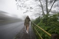 Tourist Woman walking on sidewalk alone with camera after taking picture of the fog in forest. Royalty Free Stock Photo