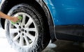 A person is washing a car tire with a green brush. Tire is covered in water and soap. Blue car wash with white soap foam. Auto Royalty Free Stock Photo