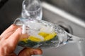 Person washing the glass by hands with a green yellow sponge full of foam in the grey sink at the kitchen and a glass cup just Royalty Free Stock Photo